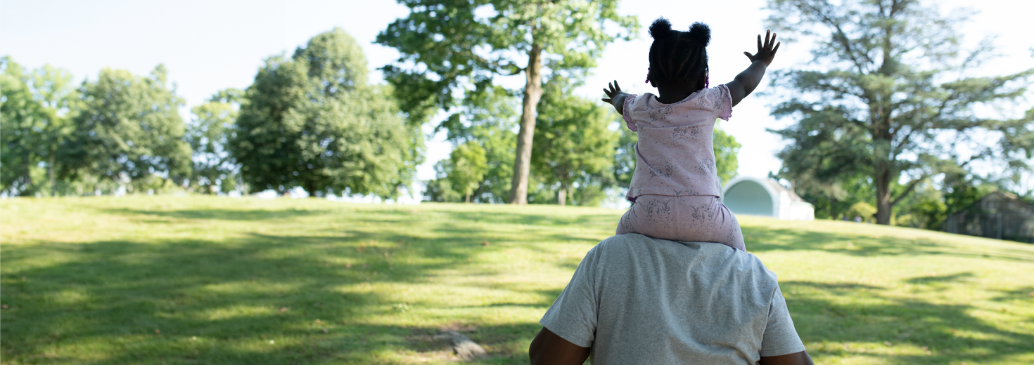 Black child riding on an adult's shoulders in a park